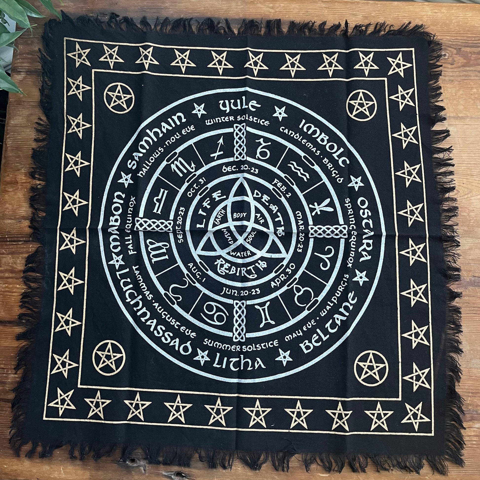 Black square Altar cloth with white Wheel of the Year symbols and text on a wooden surface