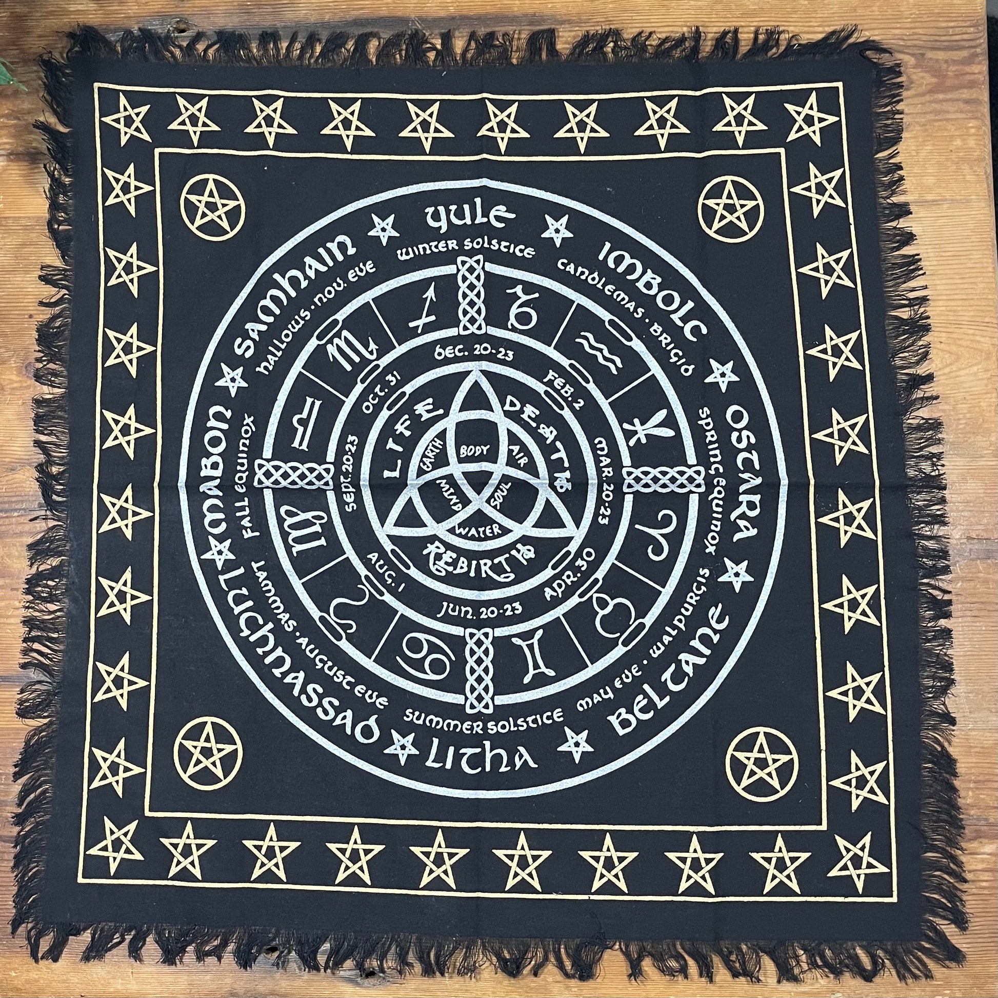 Black square Altar cloth with white Wheel of the Year symbols and text on a wooden surface