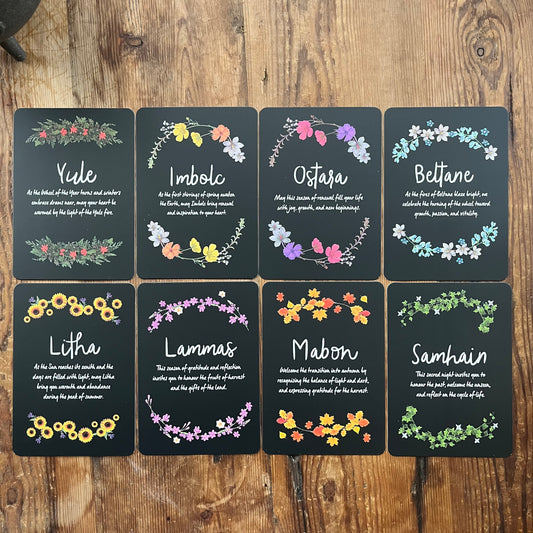 Set of eight cards with floral designs and Sabbat names on a wooden surface