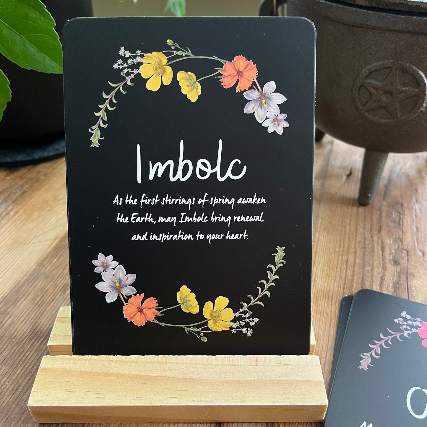Black Altar card with floral design and Imbolc text on a wooden stand.