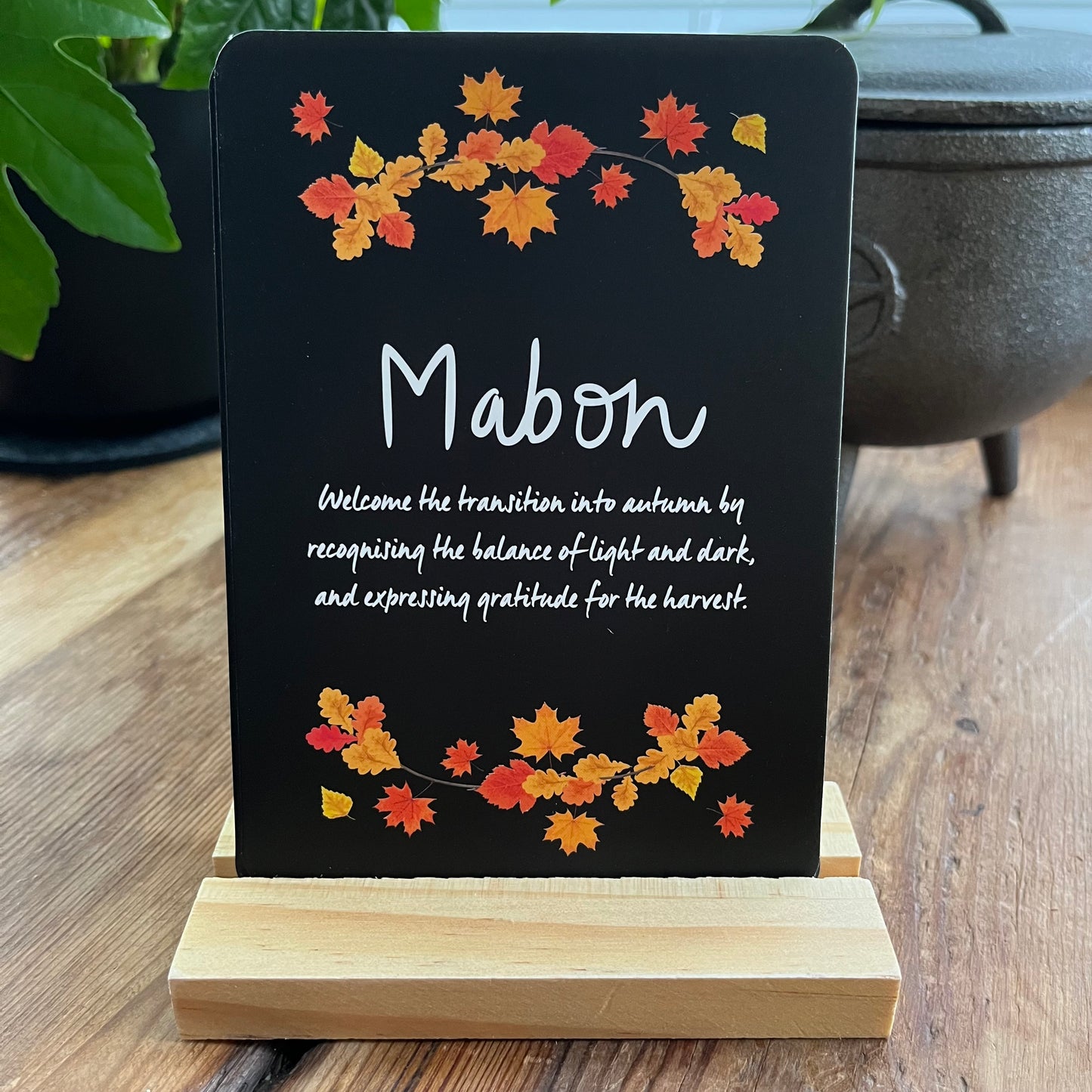 Black sign with autumn leaf design and 'Mabon' text on a wooden stand.