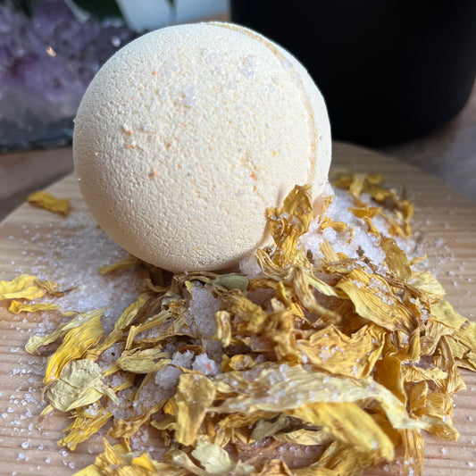 pale yellow bath bomb rested on top of yellow flower petals and white himalayan salt. 