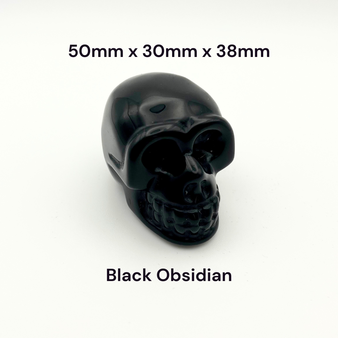 A glossy black obsidian skull-shaped bead or cabochon on a plain white background, with text overlays indicating dimensions '50mm x 30mm x 38mm' and material 'Black Obsidian'.