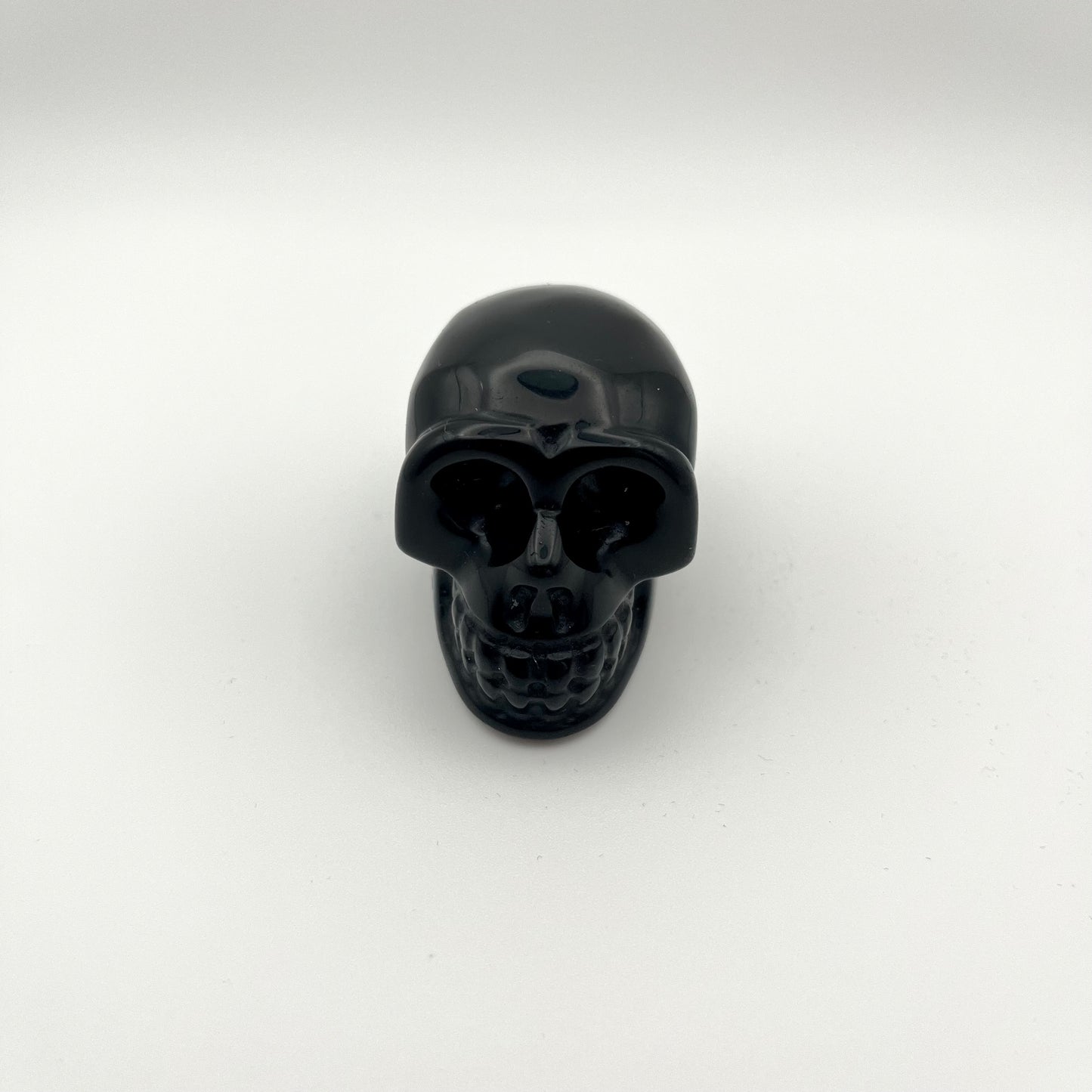 A glossy black skull-shaped crystal centered on a plain white studio background.