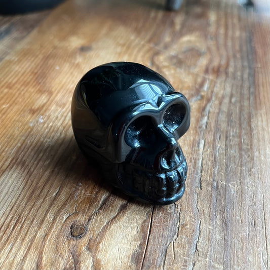 A glossy black skull-shaped object, possibly a Skull carving, resting on a rustic wooden surface.