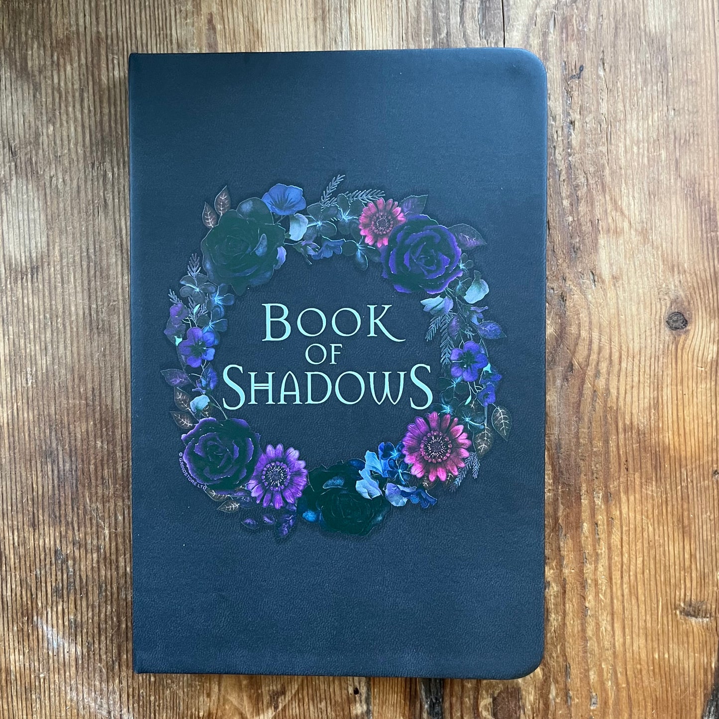 Book titled 'Book of Shadows' with floral design on a wooden surface