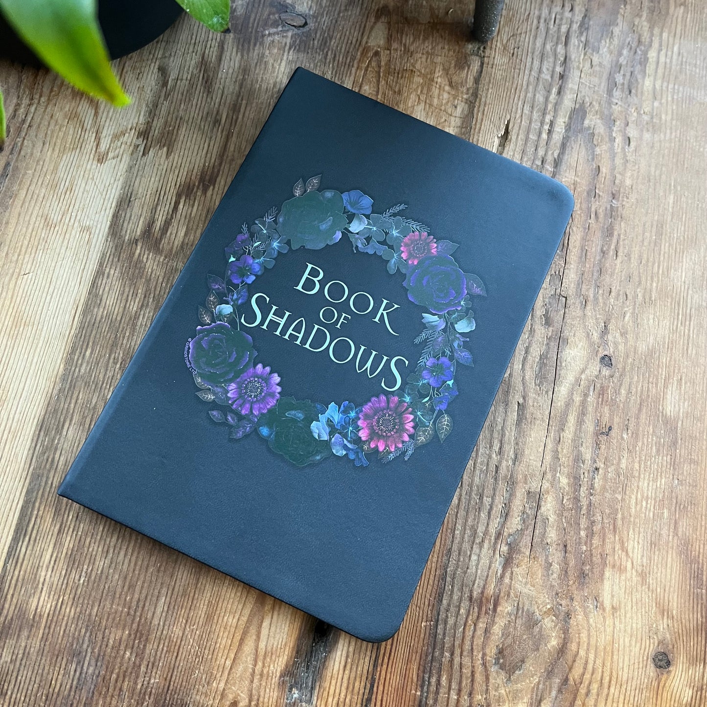 Dark blue notebook titled 'Book of Shadows' with floral design on a wooden surface