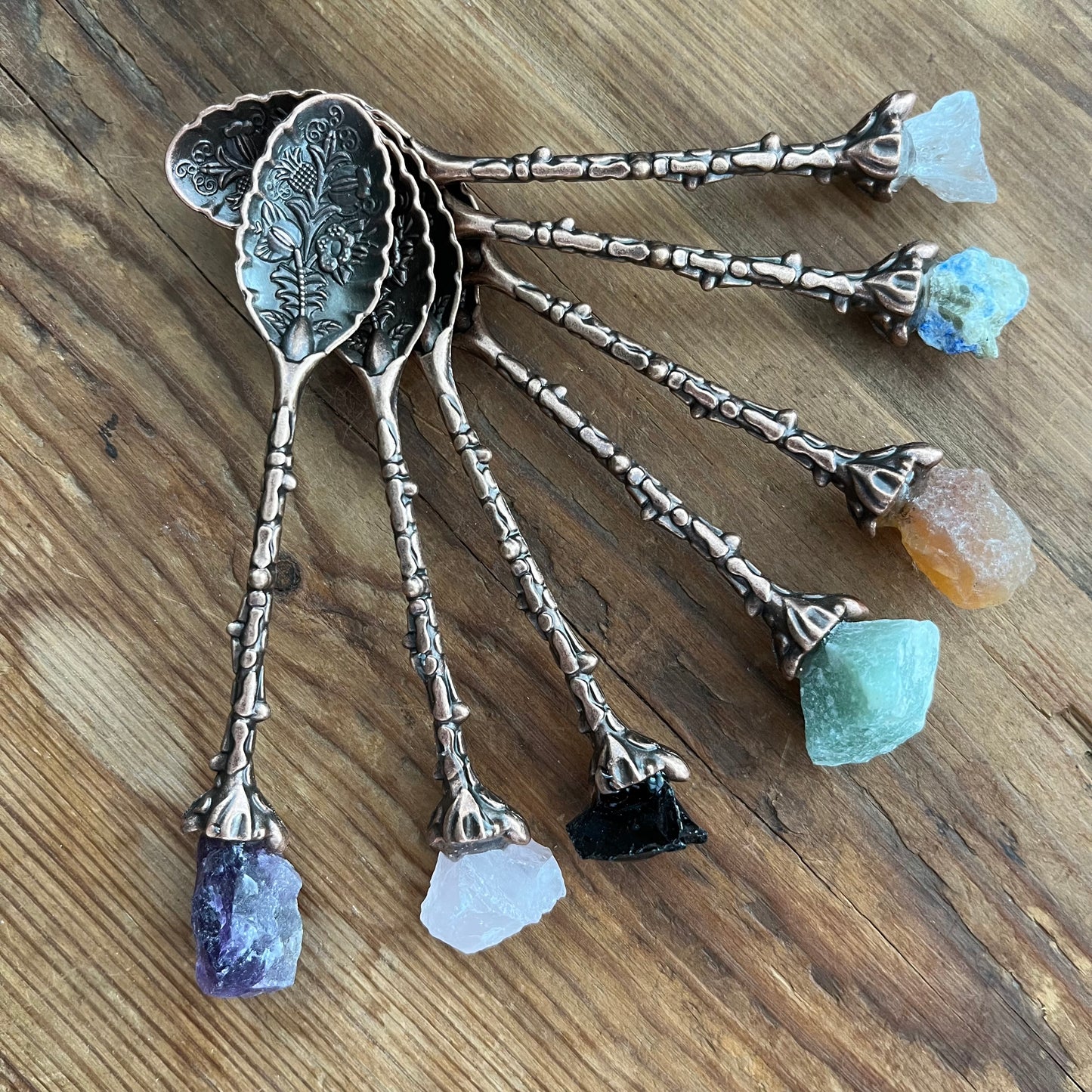Set of decorative spoons with gemstone handles on a wooden surface