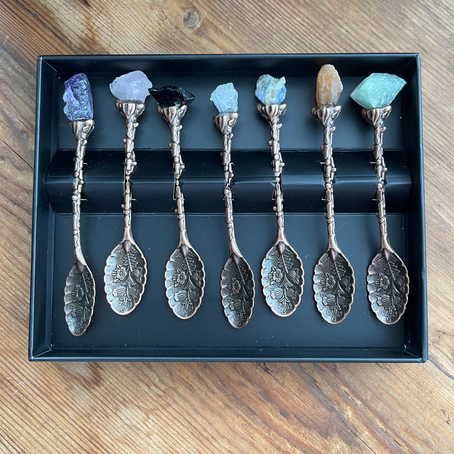 Set of silver spoons with decorative handles and gemstones on a wooden surface