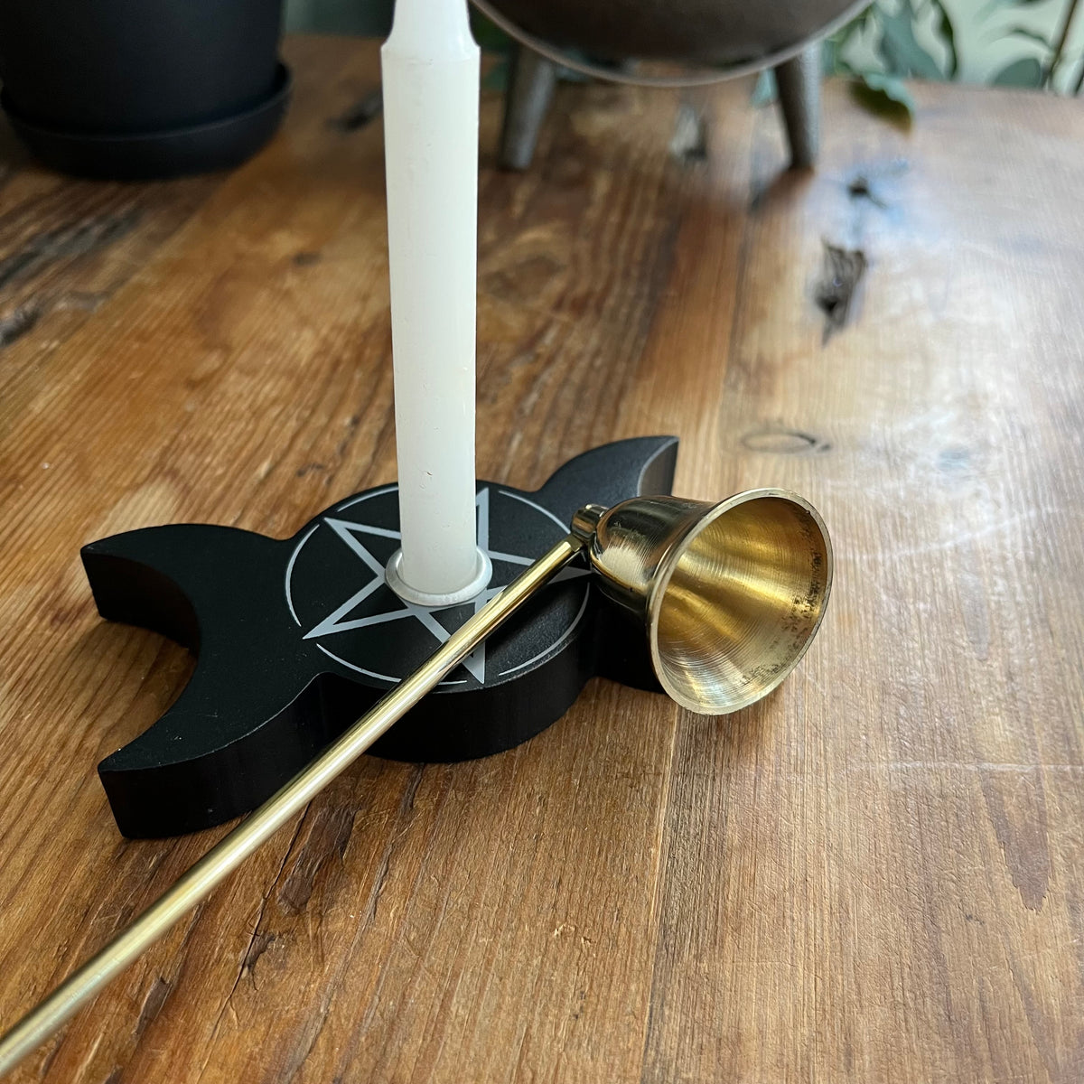 A brass pentacle candle snuffer with a white candle and holder on a rustic wooden table.