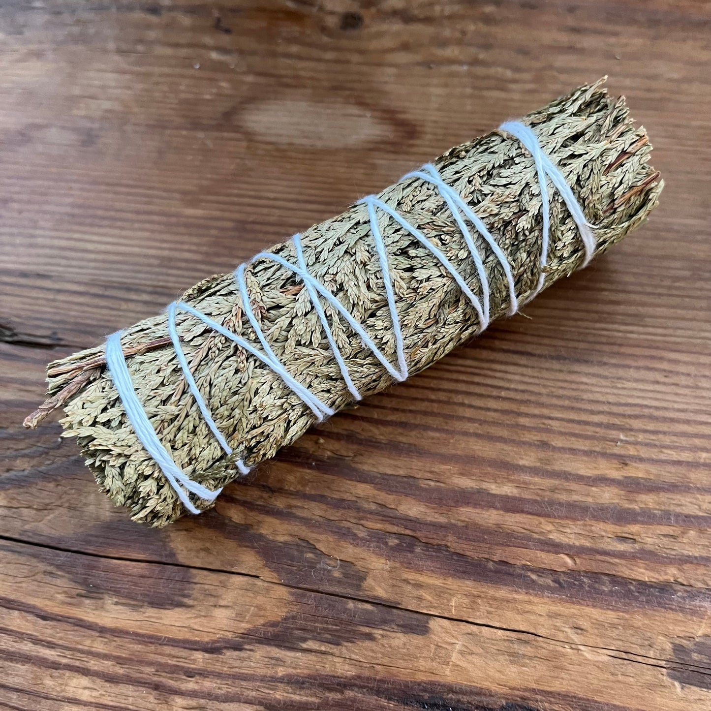 A dried sage smudge bundle wrapped with white string, placed diagonally on a rustic wooden surface.
