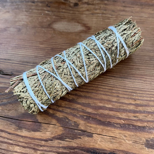 A dried sage smudge bundle wrapped with white string, placed diagonally on a rustic wooden surface.