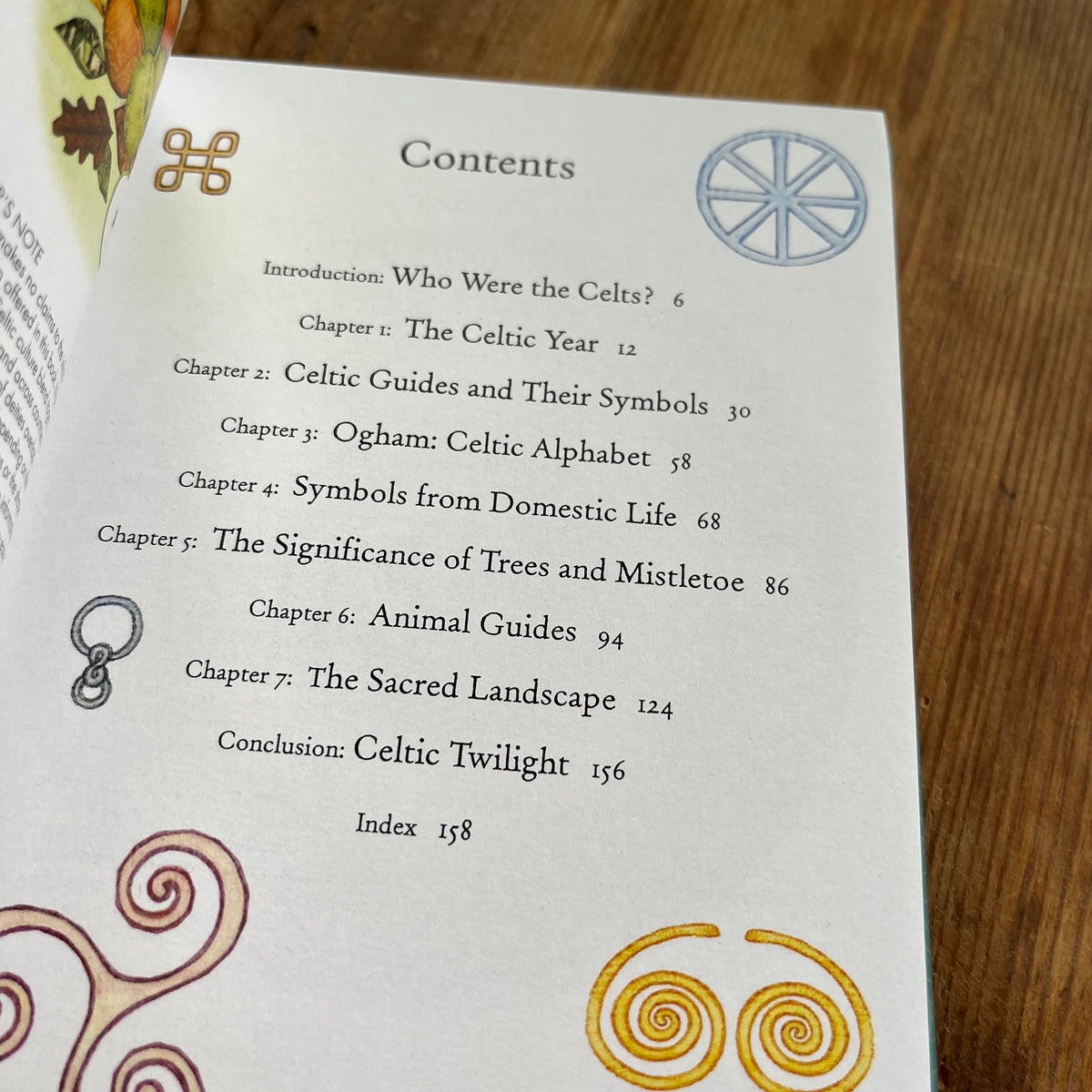 An open book showing a printed Contents page with chapter titles and decorative Celtic-style symbols, photographed on a wooden surface.