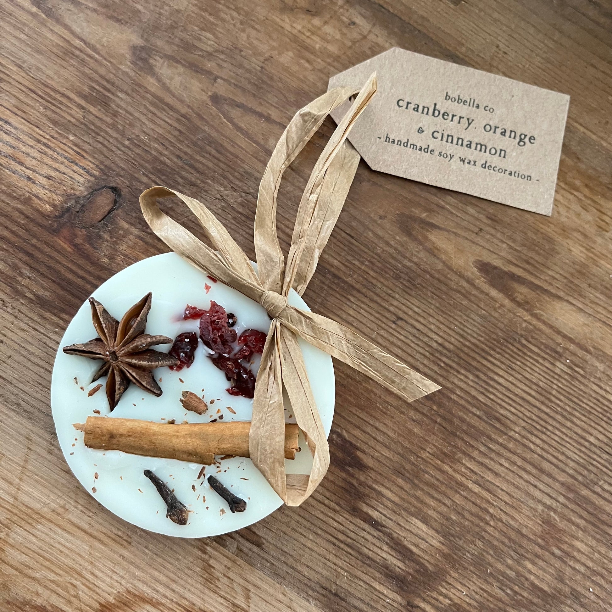 Decorative item with cinnamon stick, star anise, and cranberries on a wooden surface with a tag.