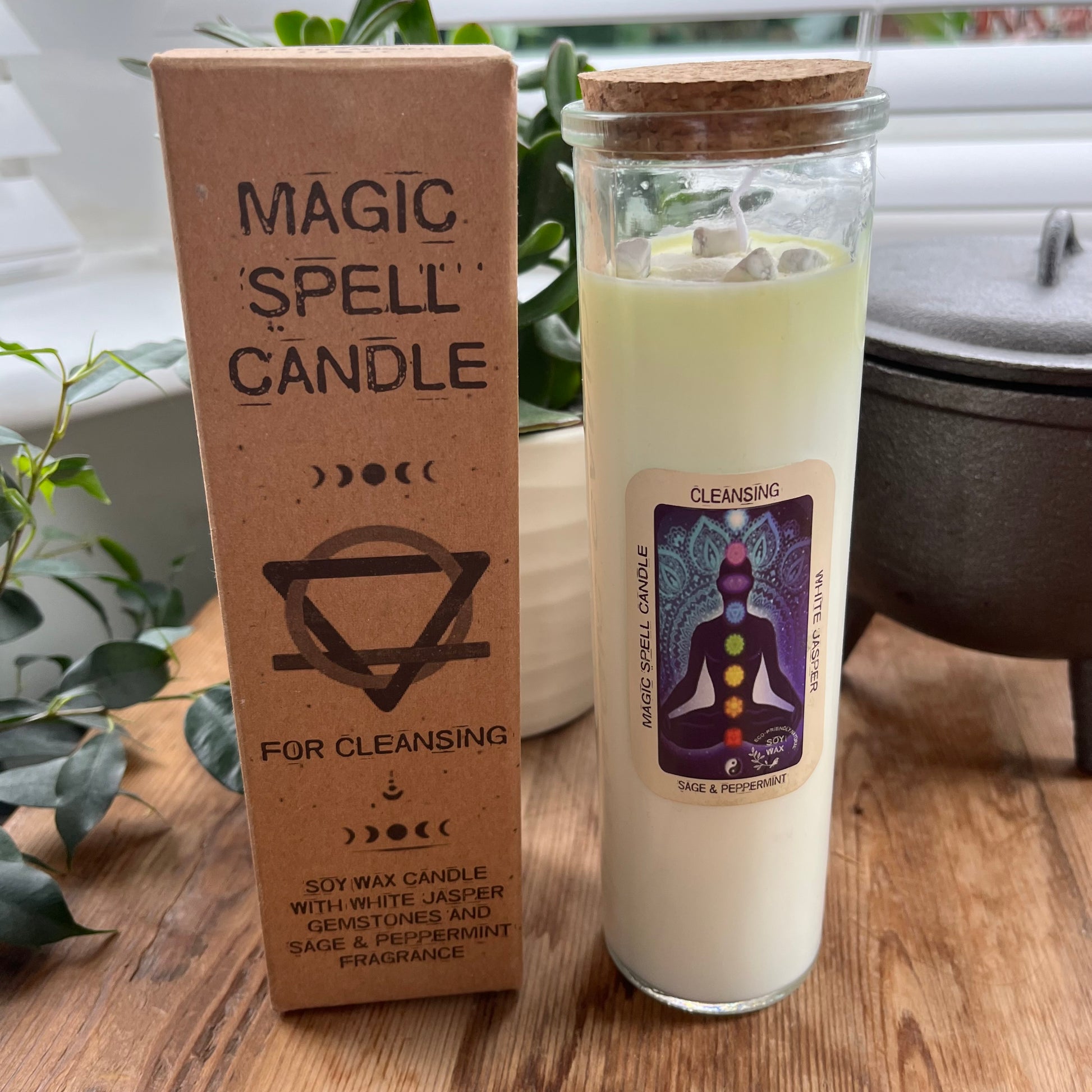 Tall glass spell candle with cork lid. The label on the candle features an image of a seated person and their coloured chakras  and the words Magic spell candle, Cleansing, white Jasper and Sage and Peppermint. The candle itself is white with white Jasper gemstones embedded within it. Alongside the glass Magic spell candle is it's brown cardboard box which has the words magic spell candle for Cleansing, soy wax candle with white Jasper gemstones and sage and peppermint  fragrance.