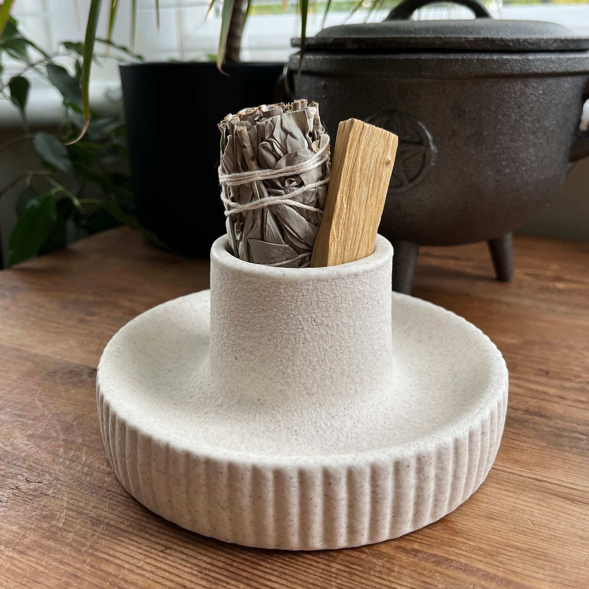 White ceramic holder with incense sticks and a wrapped sage bundle on a wooden surface.