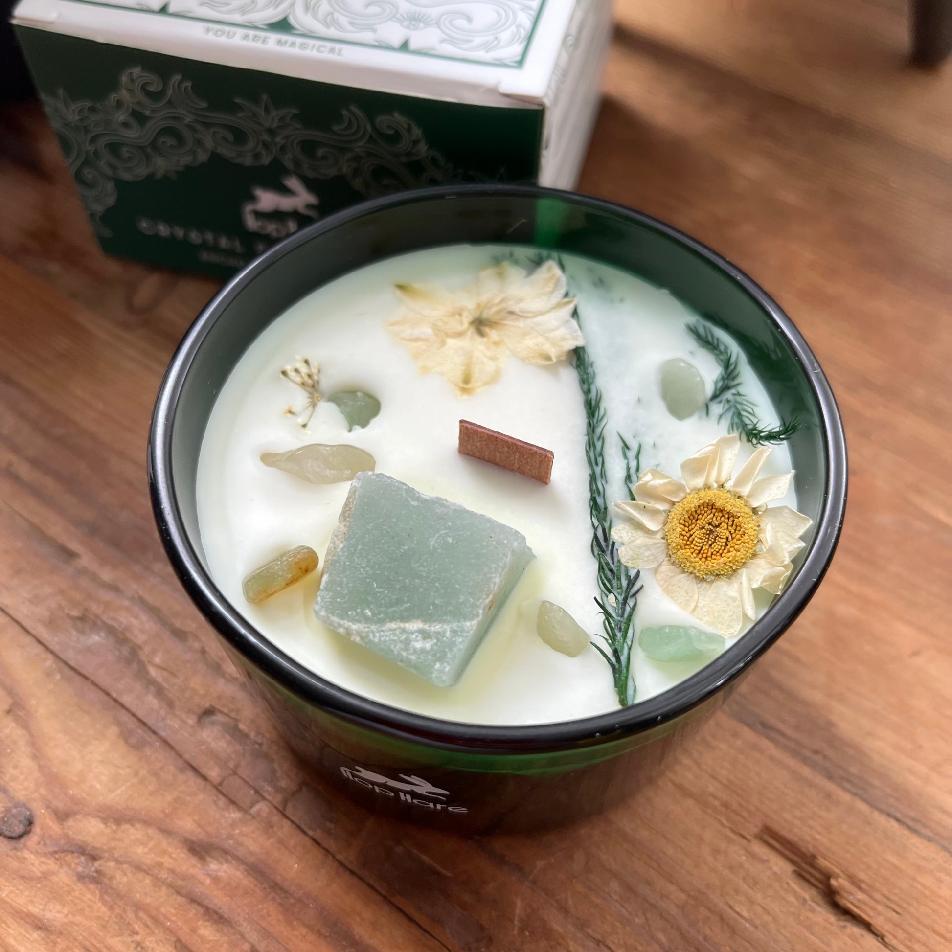 Decorative candle with flowers and herbs in a container on a wooden surface