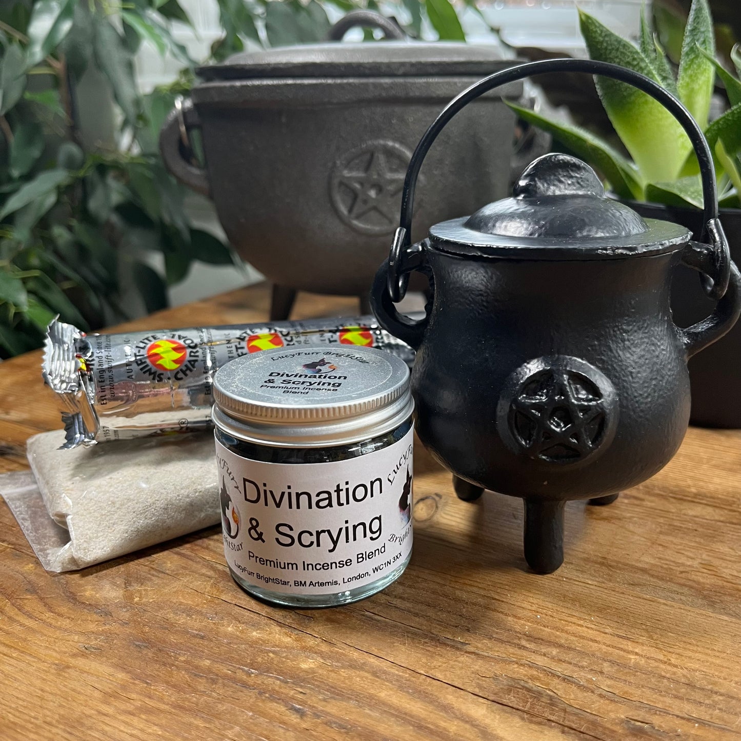 Incense container labeled 'Divination & Scrying' next to a black cauldron with pentacle design on a wooden surface.