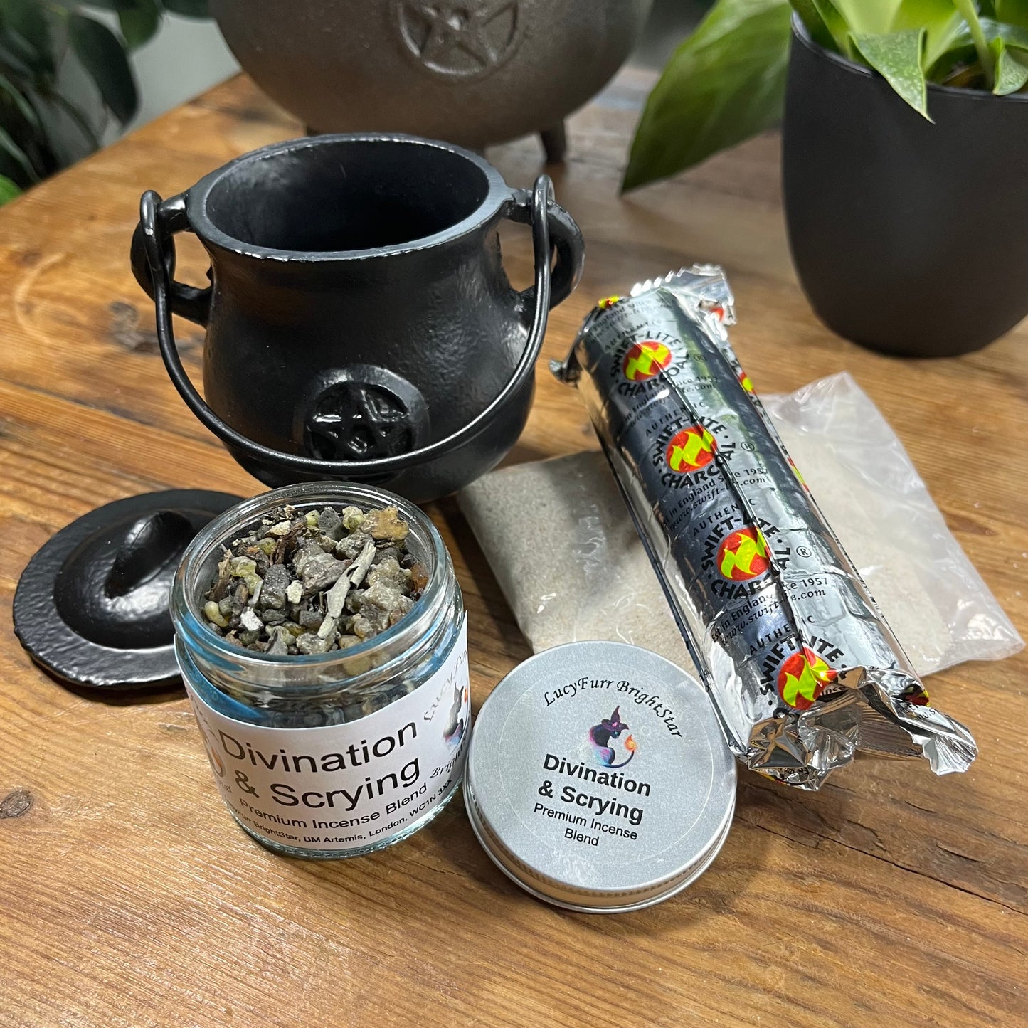 A black cauldron, jar labeled 'Divination & Scrying', charcoal discs and cauldron sand on a wooden surface