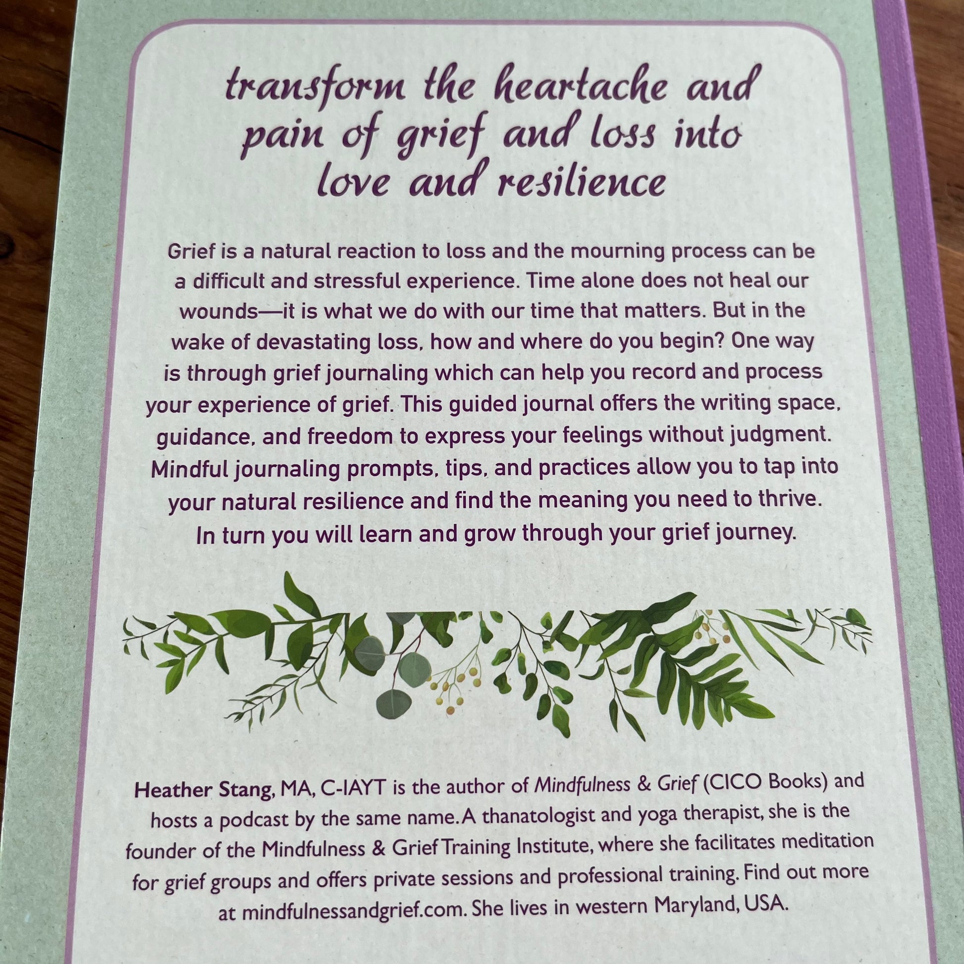 The back cover of a journal showing a lavender and mint green background with purple text that reads 'transform the heartache and pain of grief and loss into love and resilience,' plus a short description, decorative leaf illustration, and Heather Ma's contact information.