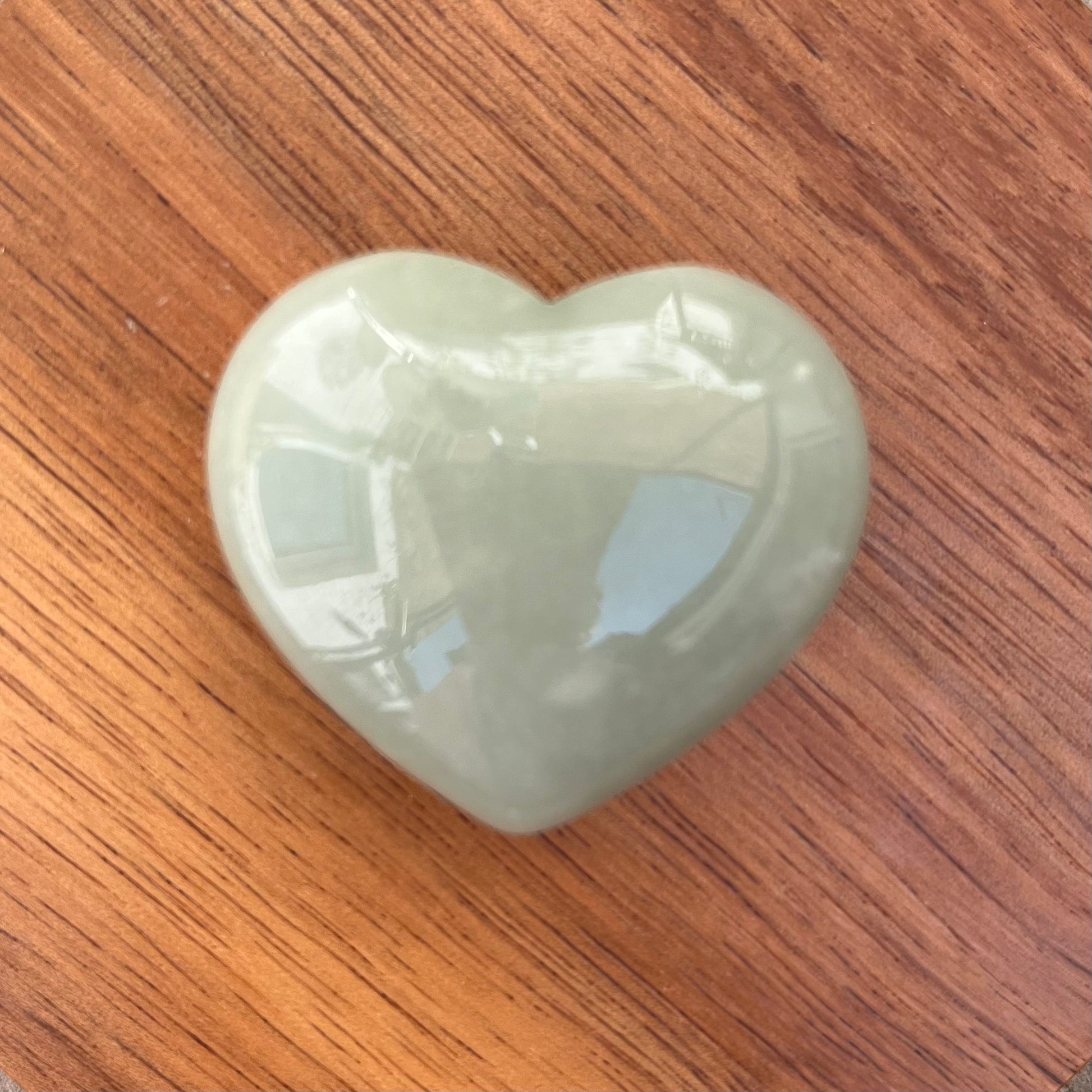 A polished light green heart-shaped stone or crystal resting on a brown wooden surface.