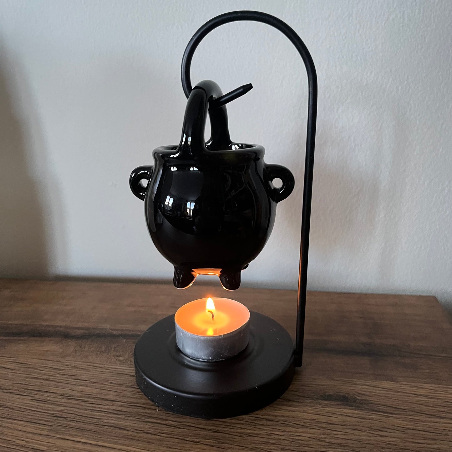Black cauldron-shaped loil burner with a lit candle on a wooden surface