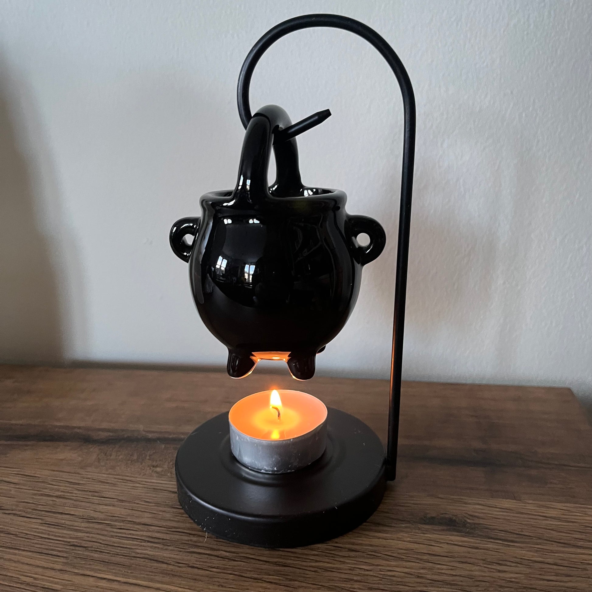Black cauldron-shaped loil burner with a lit candle on a wooden surface