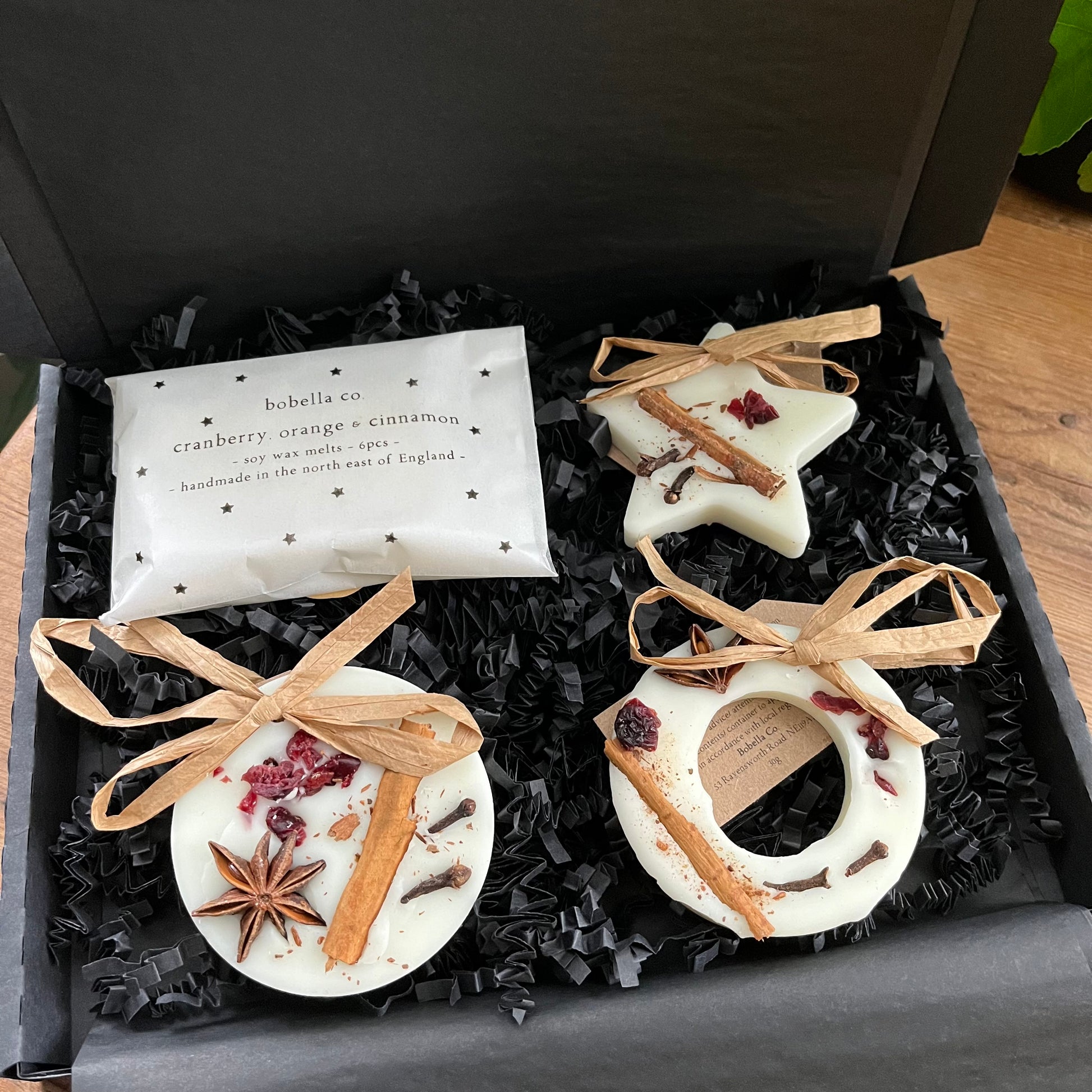 Three festive shaped hanging wax melt decorations and a pack of mini wax melts n a gift box,  on a wooden surface.  