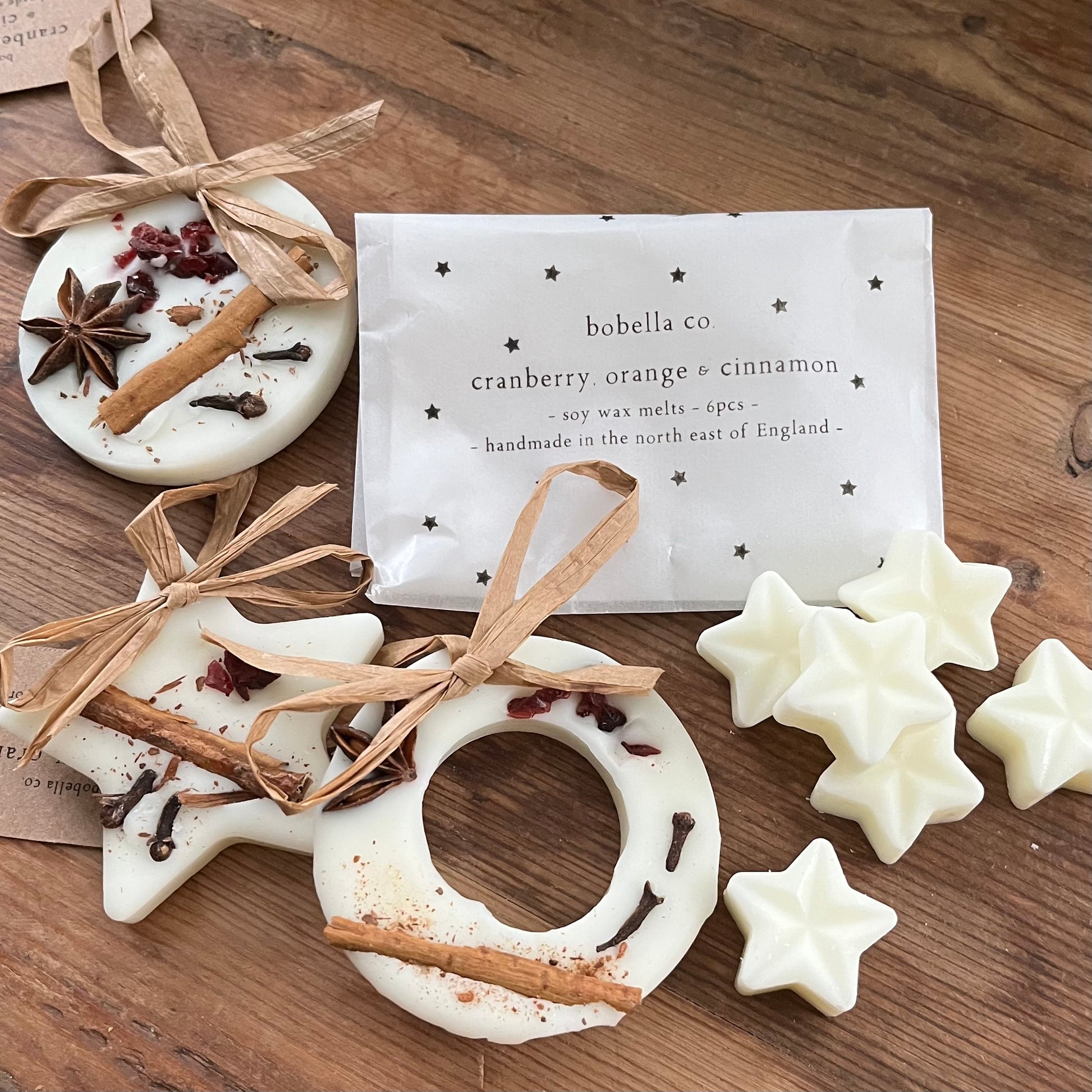 Decorative wax melts with star and circular shapes, tied with ribbons, on a wooden surface with a bobella co packaging.