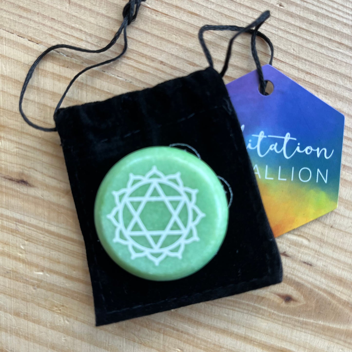 Green circular flat meditation stone is engraved with the Heart Chakra symbol alongside it's black velvet pouch 