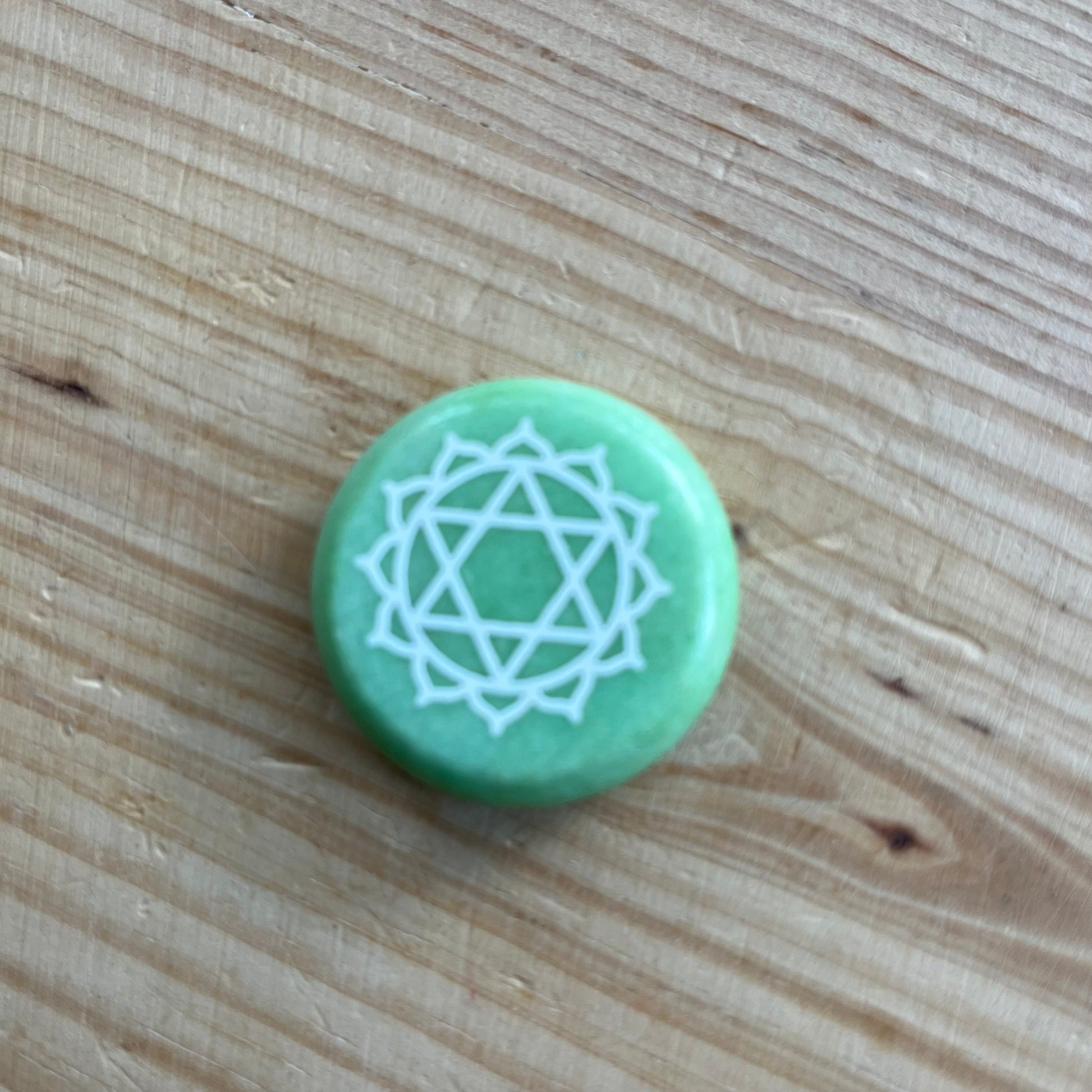 Green circular flat meditation stone is engraved with the Heart Chakra symbol 