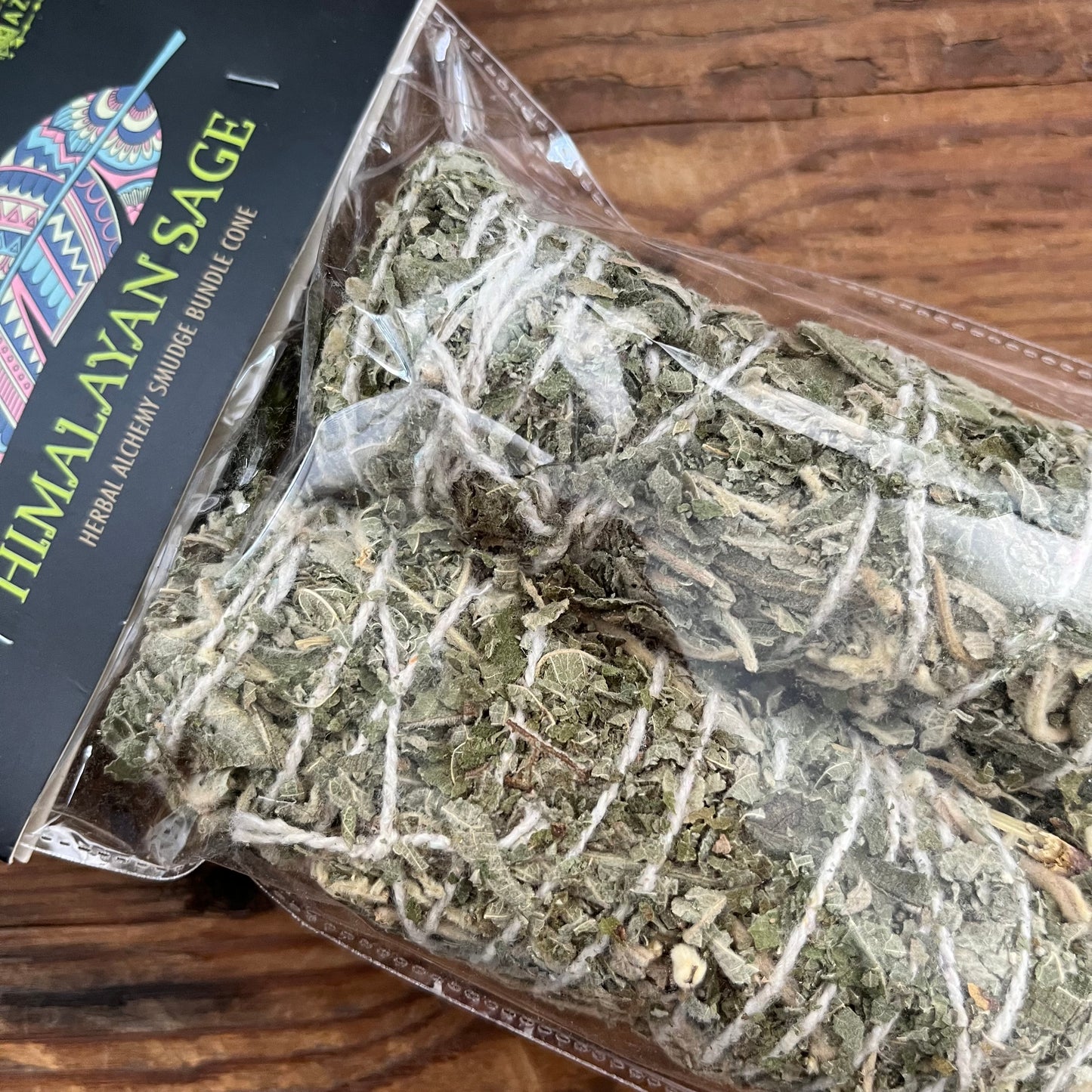 A packaged bundle of dried Himalayan sage herb, shown inside a clear plastic bag with a black branded label, placed on a wooden surface.