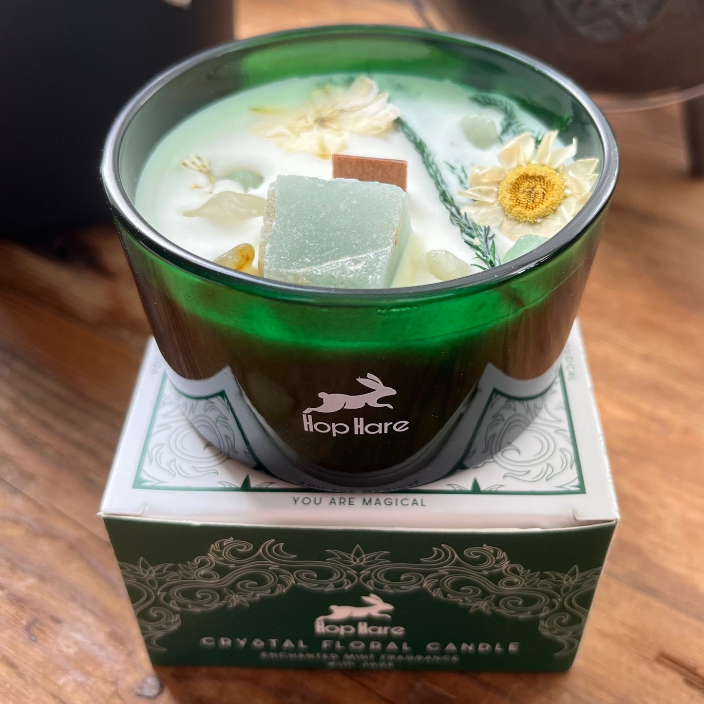 Crystal floral candle in a green container with 'hop hare' branding on a wooden surface.