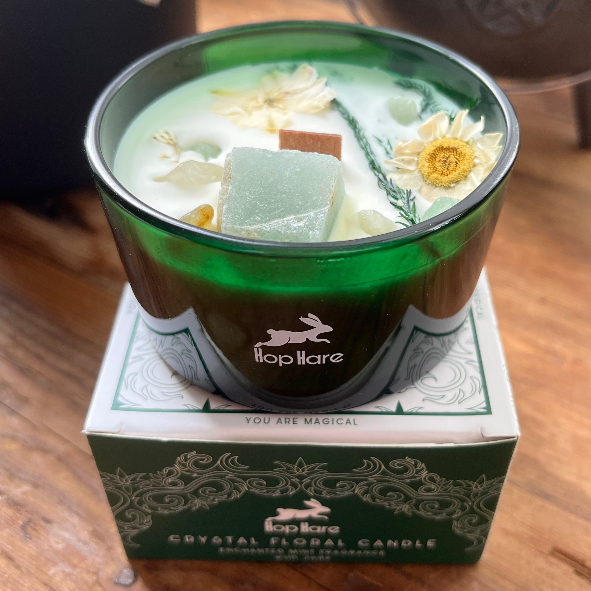 Crystal floral candle in a green container with 'hop hare' branding on a wooden surface.