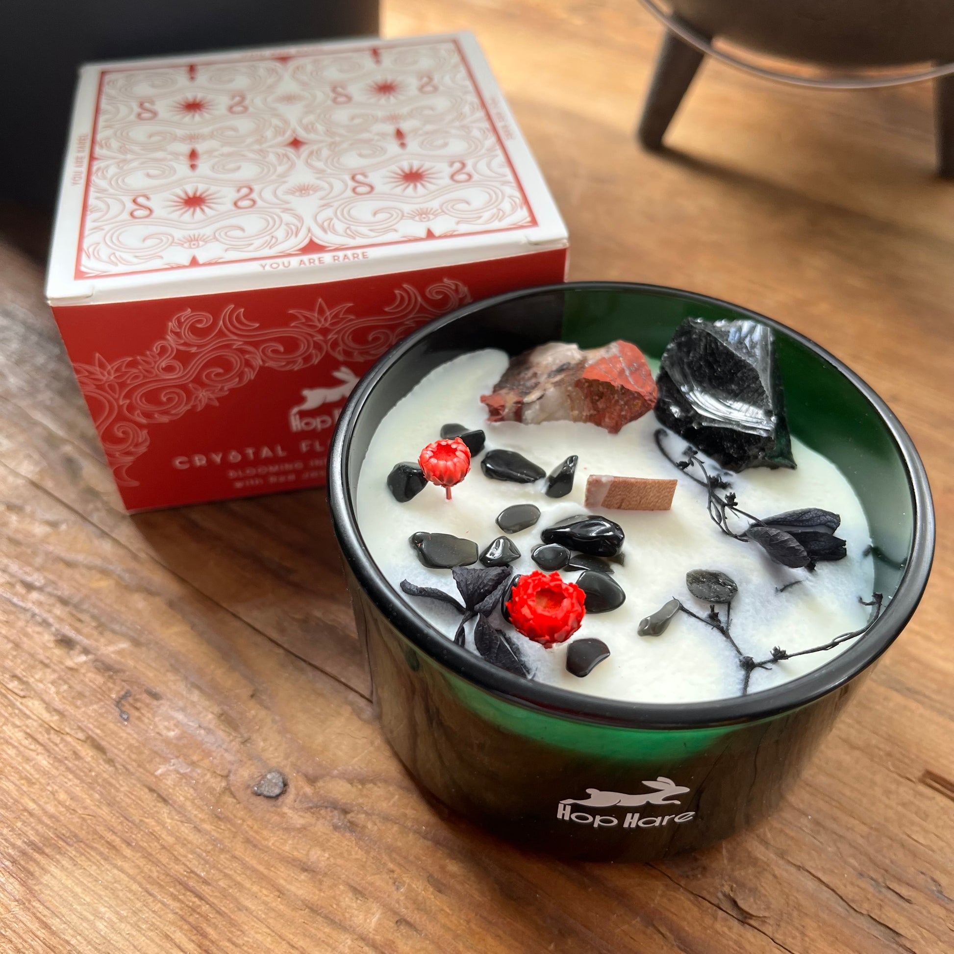 Candle with decorative elements in a green container on a wooden surface, next to a red box.
