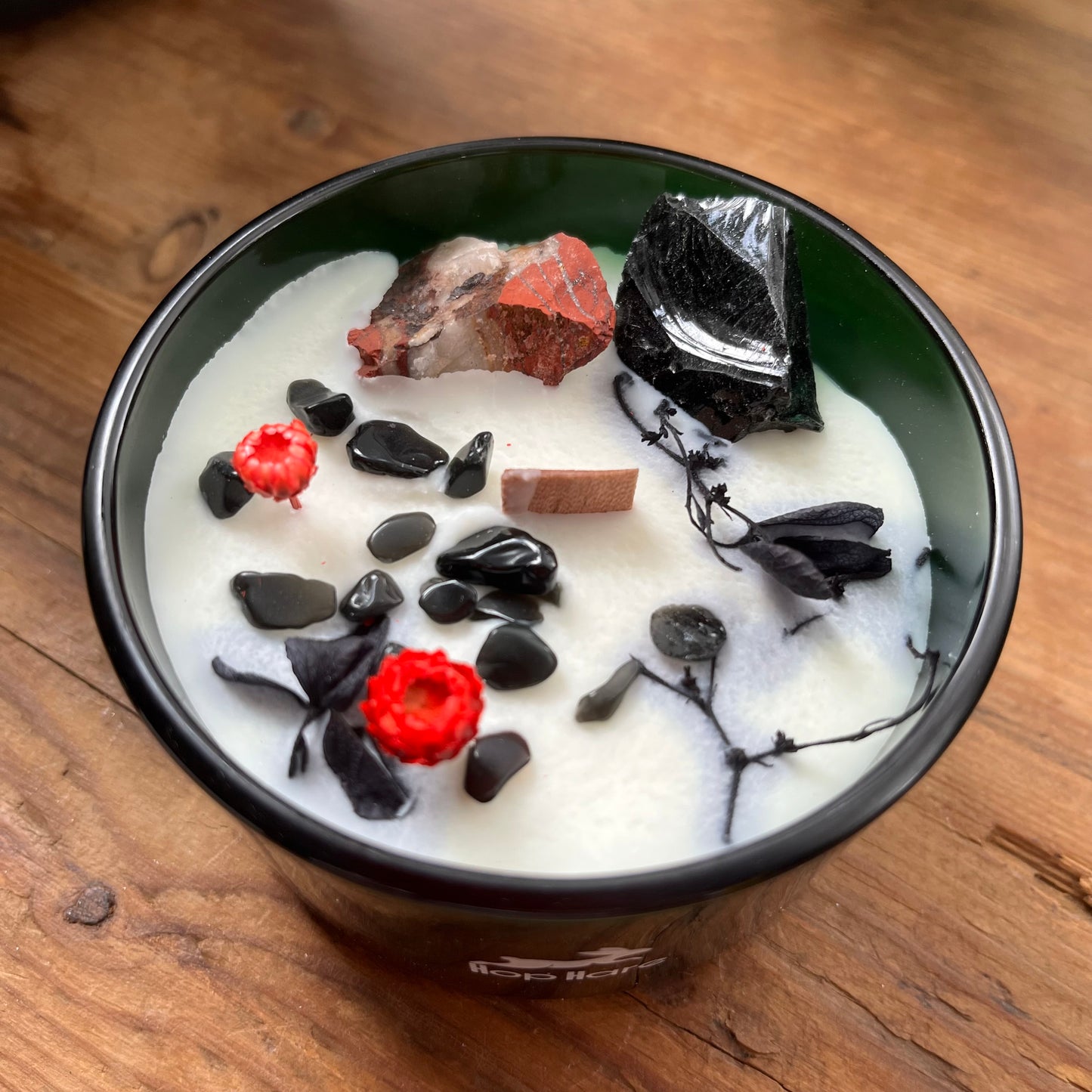 candle decorated with black and red crystals, red flowers, on a wooden surface