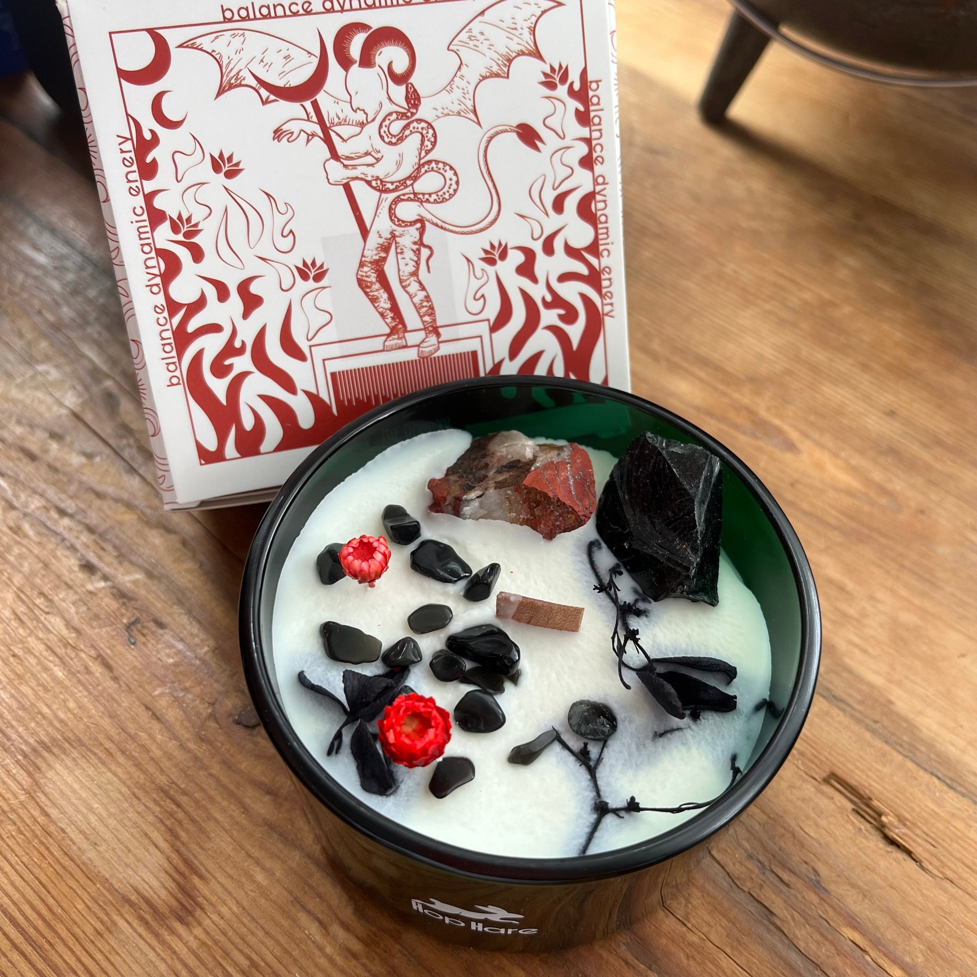 Candle in a green glass container with decorative elements on a wooden surface, next to a Devil tarot card