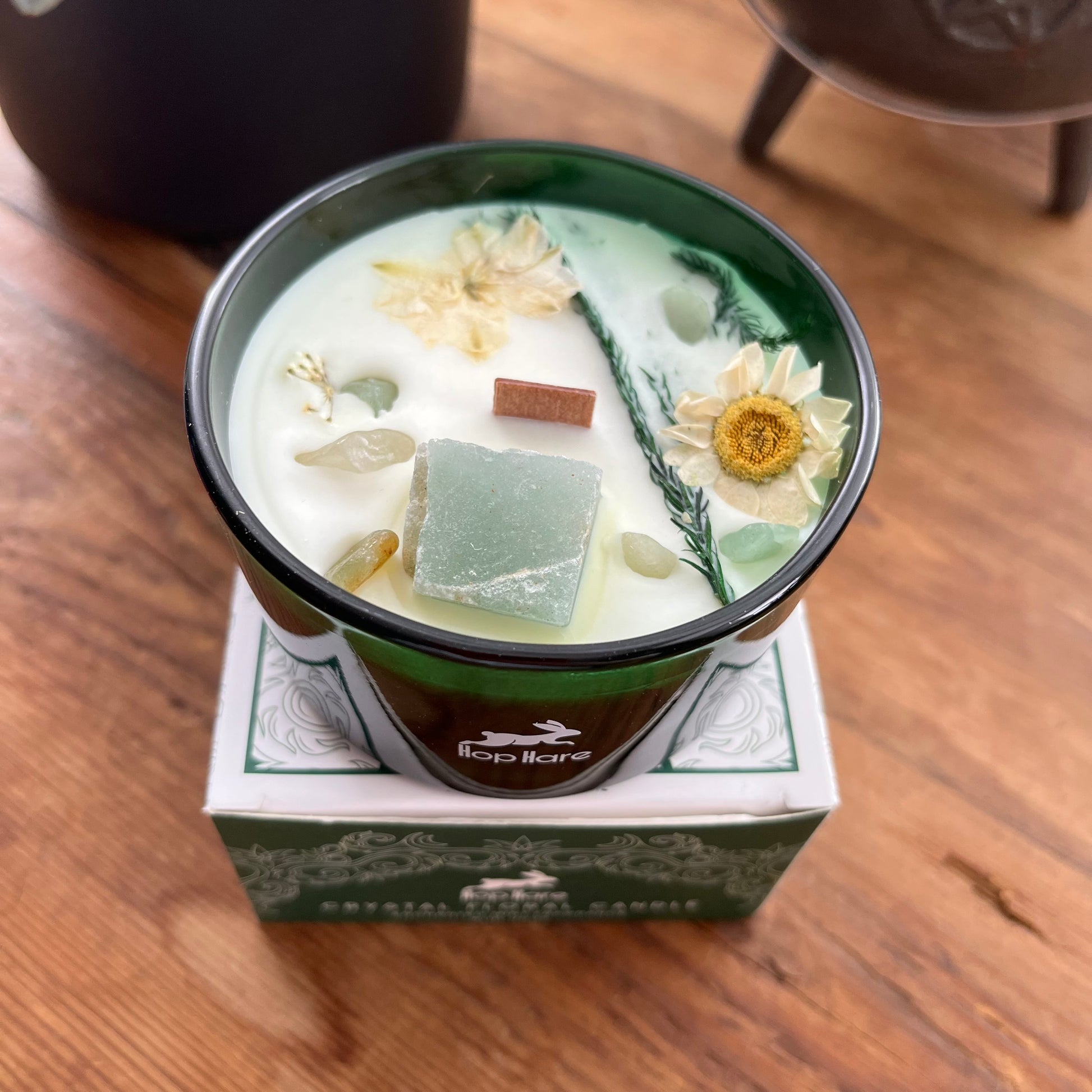 Decorative candle with flowers and herbs in a green container on a wooden surface