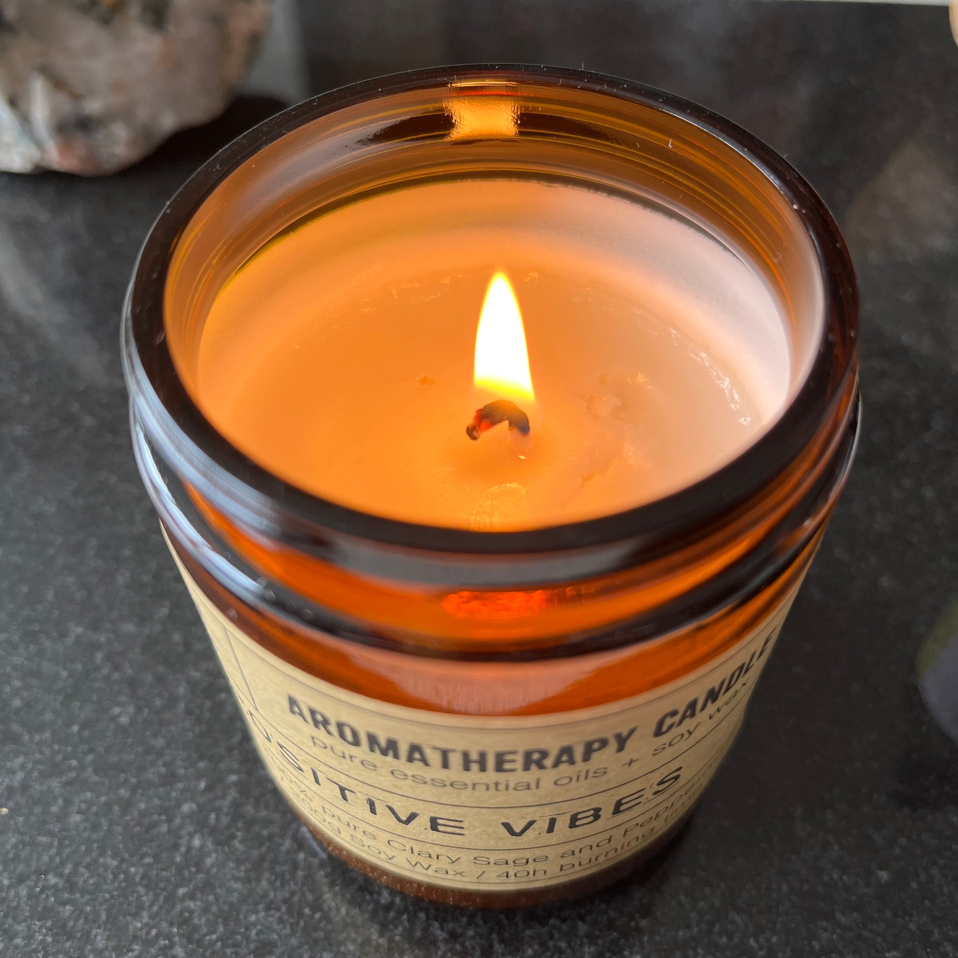 Aromatherapy candle labeled 'Sensitive Vibes' with a flame on a dark surface.