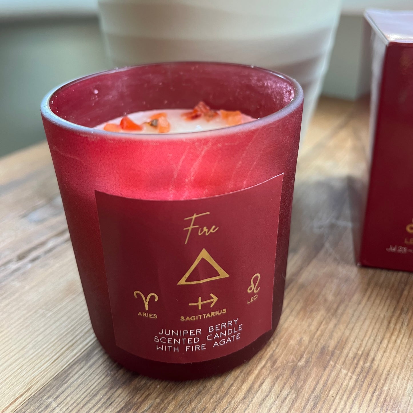 'Fire element candle' A red glass candle holder featuring the word fire and the symbol for the element of fire plus the symbols for the firey zodiac signs of Aries, Sagittarius and Leo. The candle itself is whiite with red agate crystals scattered on top.