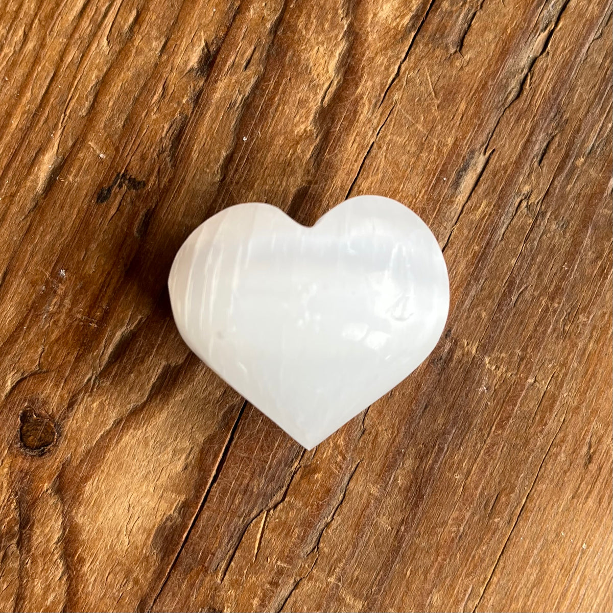A polished white heart-shaped Selenite stone, resting on a rustic brown wooden surface.