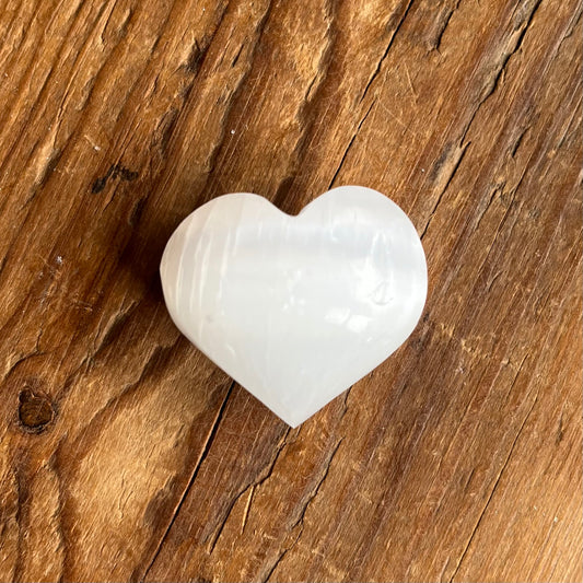 A polished white heart-shaped Selenite stone, resting on a rustic brown wooden surface.