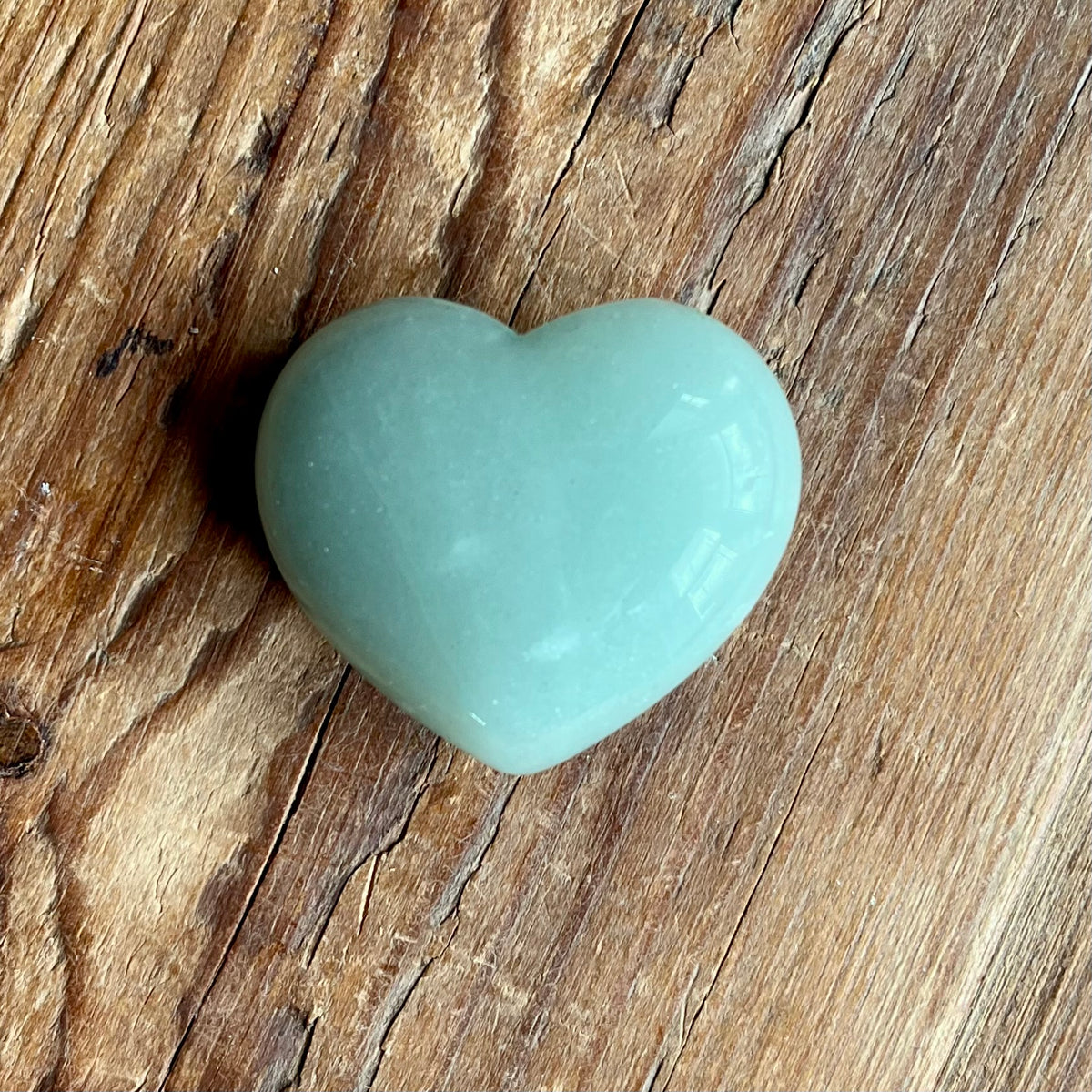 A smooth, polished light green heart-shaped stone, resting on a rustic brown wooden surface.
