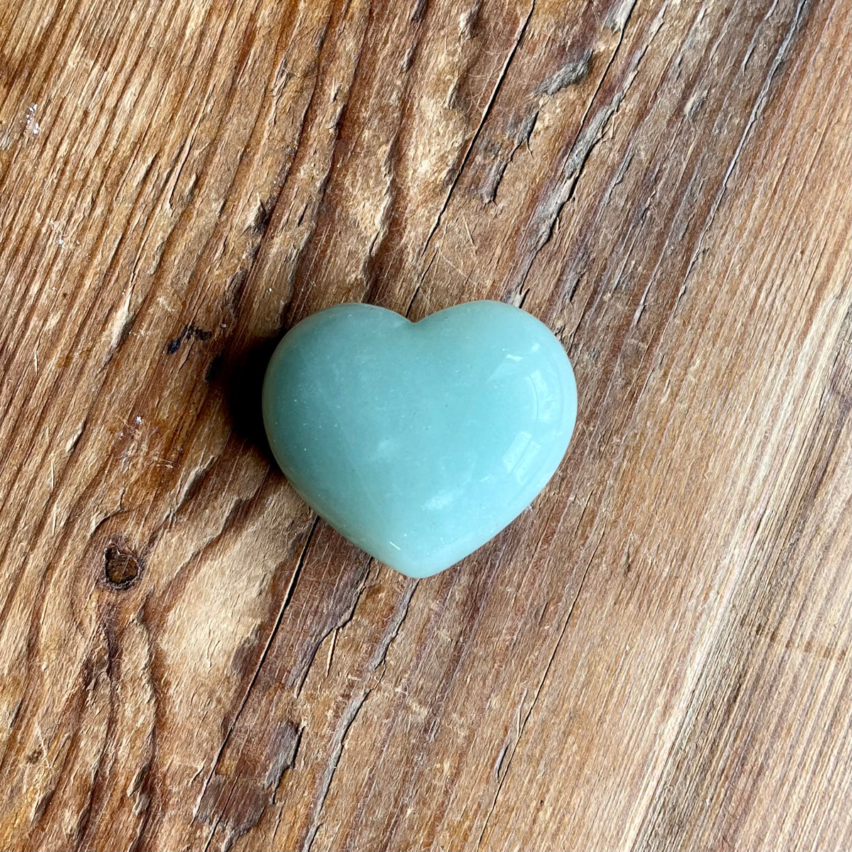 A smooth, polished light blue-green heart-shaped stone, resting on a rustic brown wooden surface.