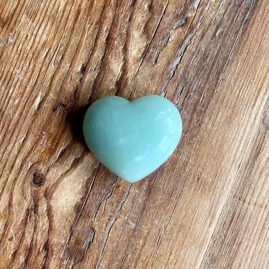 A smooth, polished light blue-green heart-shaped stone, resting on a rustic brown wooden surface.