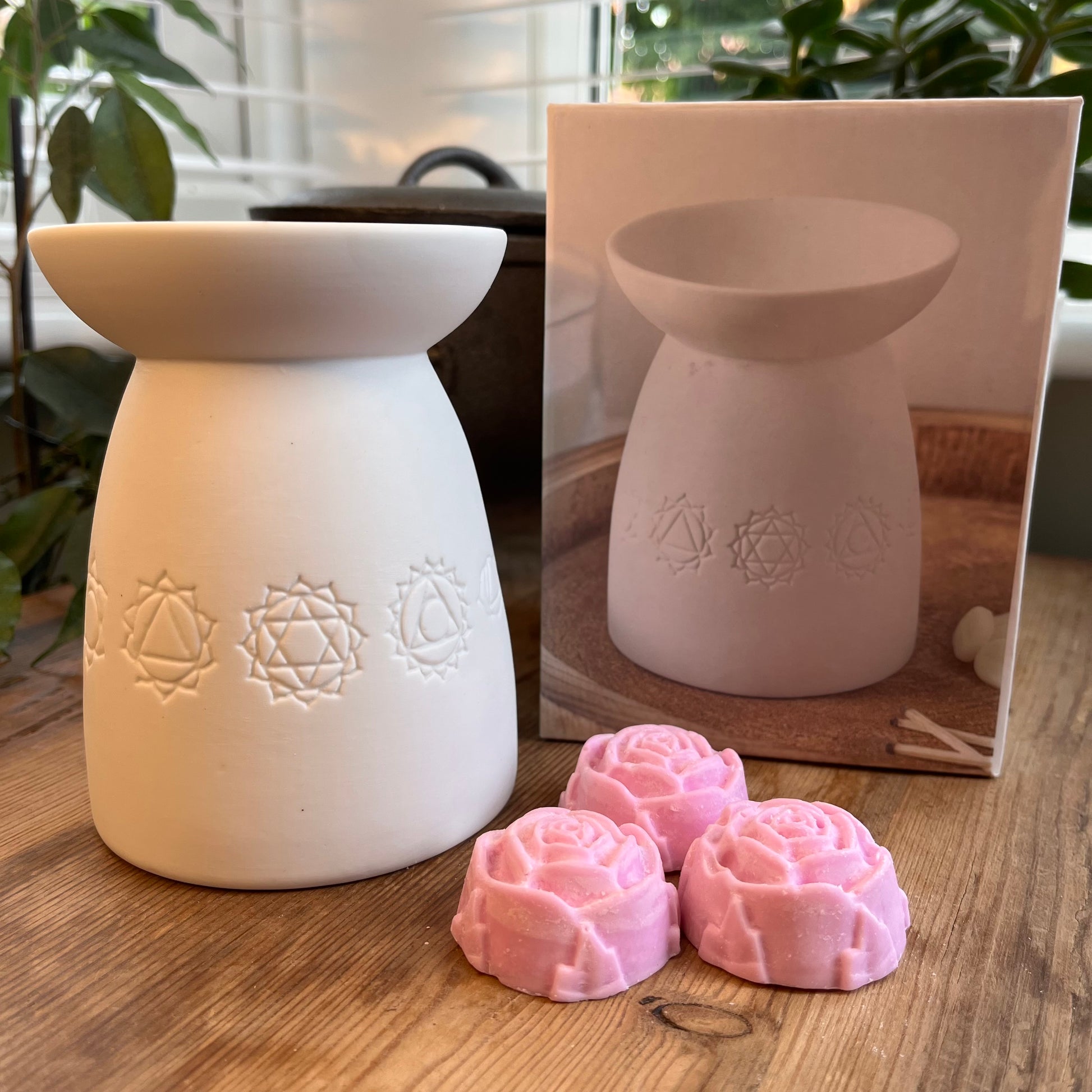 White ceramic oil burner with the symbols of the seven chakras itched around it. Pictured next to wax melts