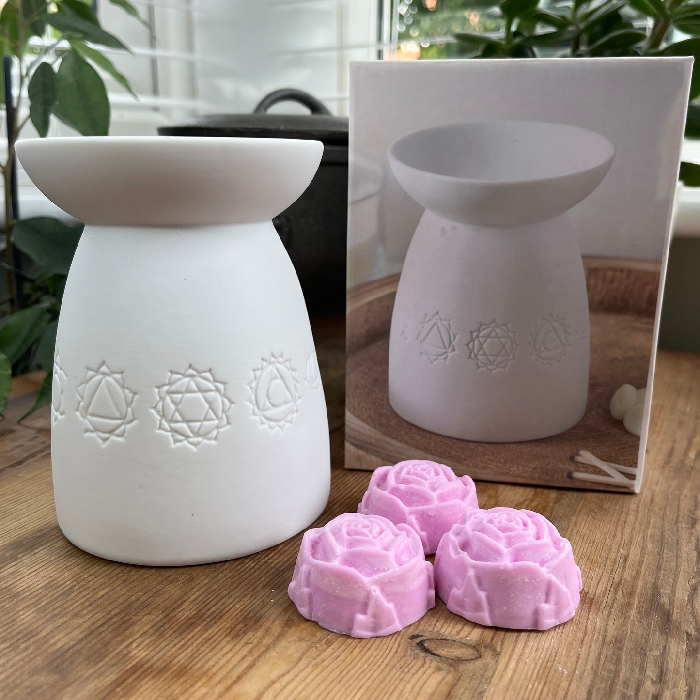 White ceramic oil burner with the symbols of the seven chakras itched around it. Pictured next to wax melts