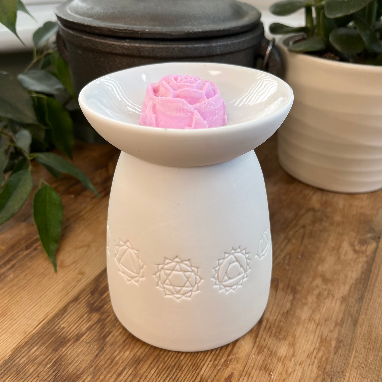 White ceramic oil burner with the symbols of the seven chakras itched around it. Pictured next to wax melts