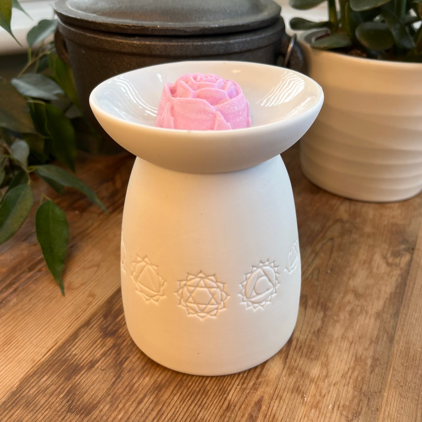 White ceramic oil burner with the symbols of the seven chakras itched around it. Pictured next to wax melts