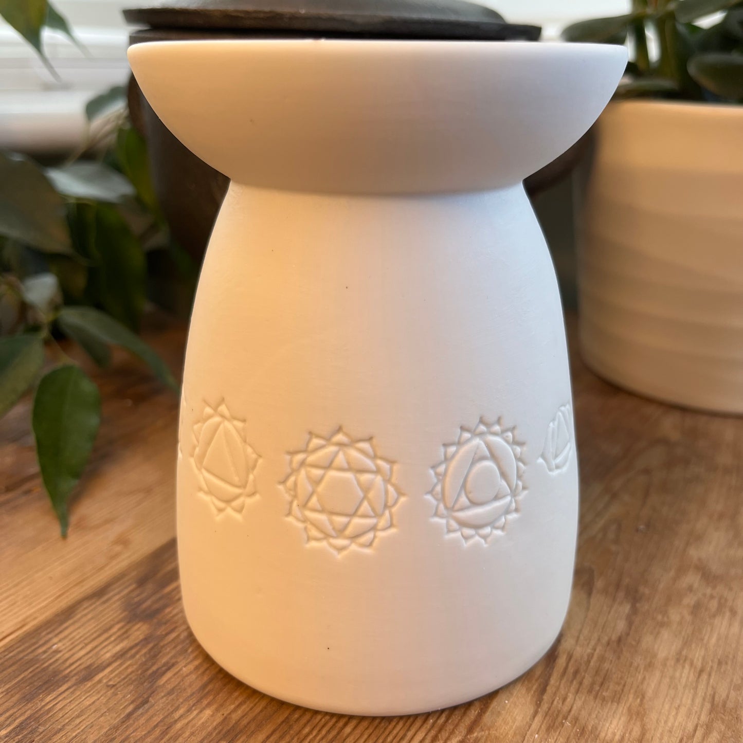 White ceramic oil burner with the symbols of the seven chakras itched around it. 